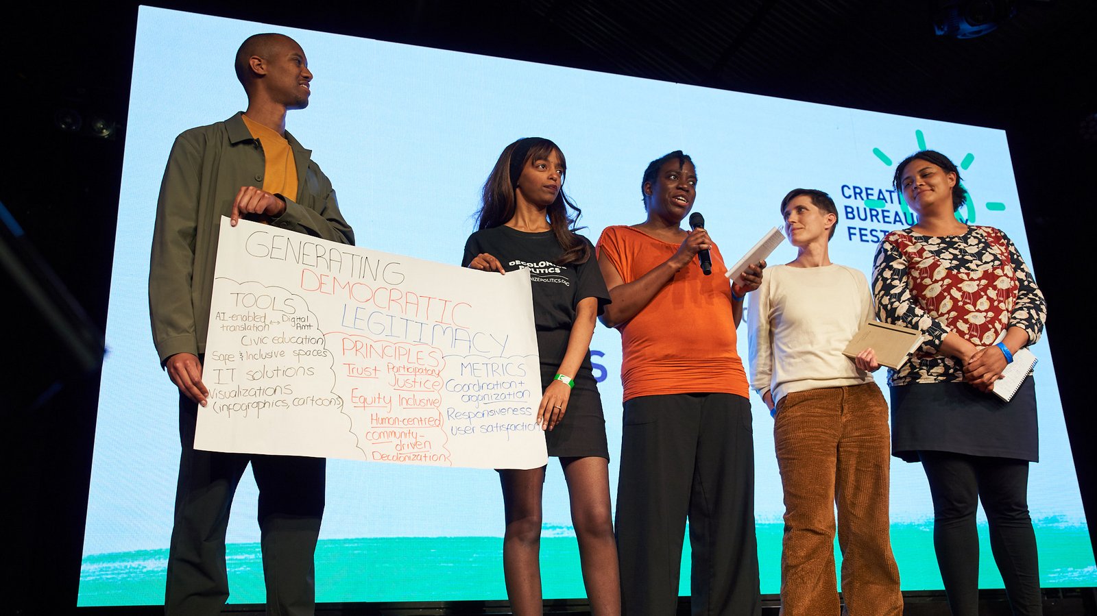 a group of 5 individuals present a poster on stage