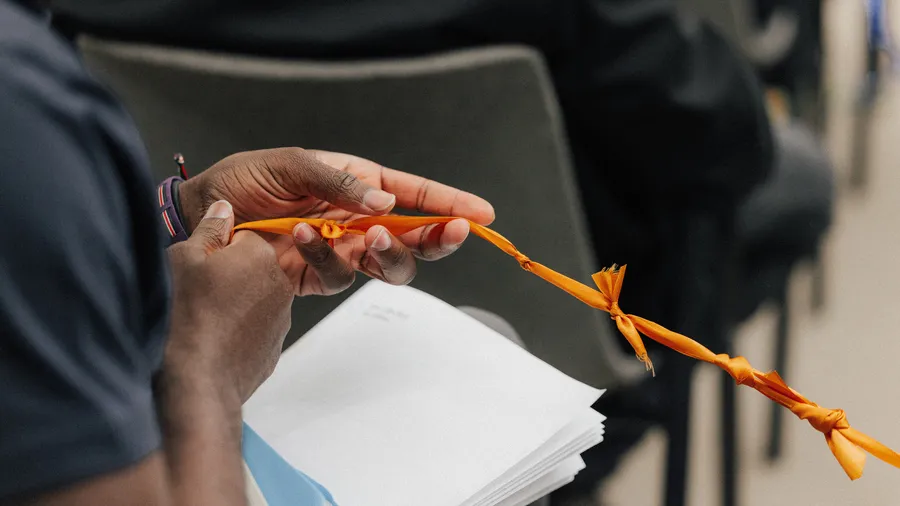 A man's hand holds a long orange string, symbolizing a connection to others.