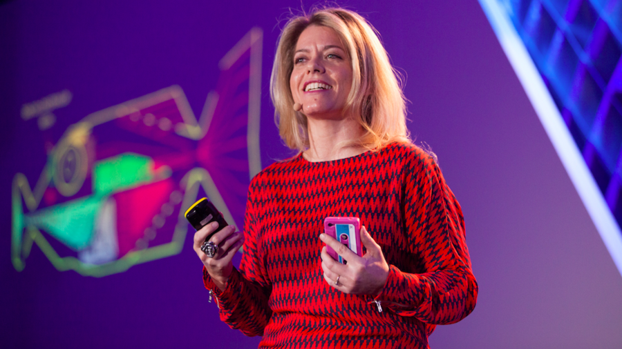 Louise Schaper holding a microphone and smiling, while giving a talk.