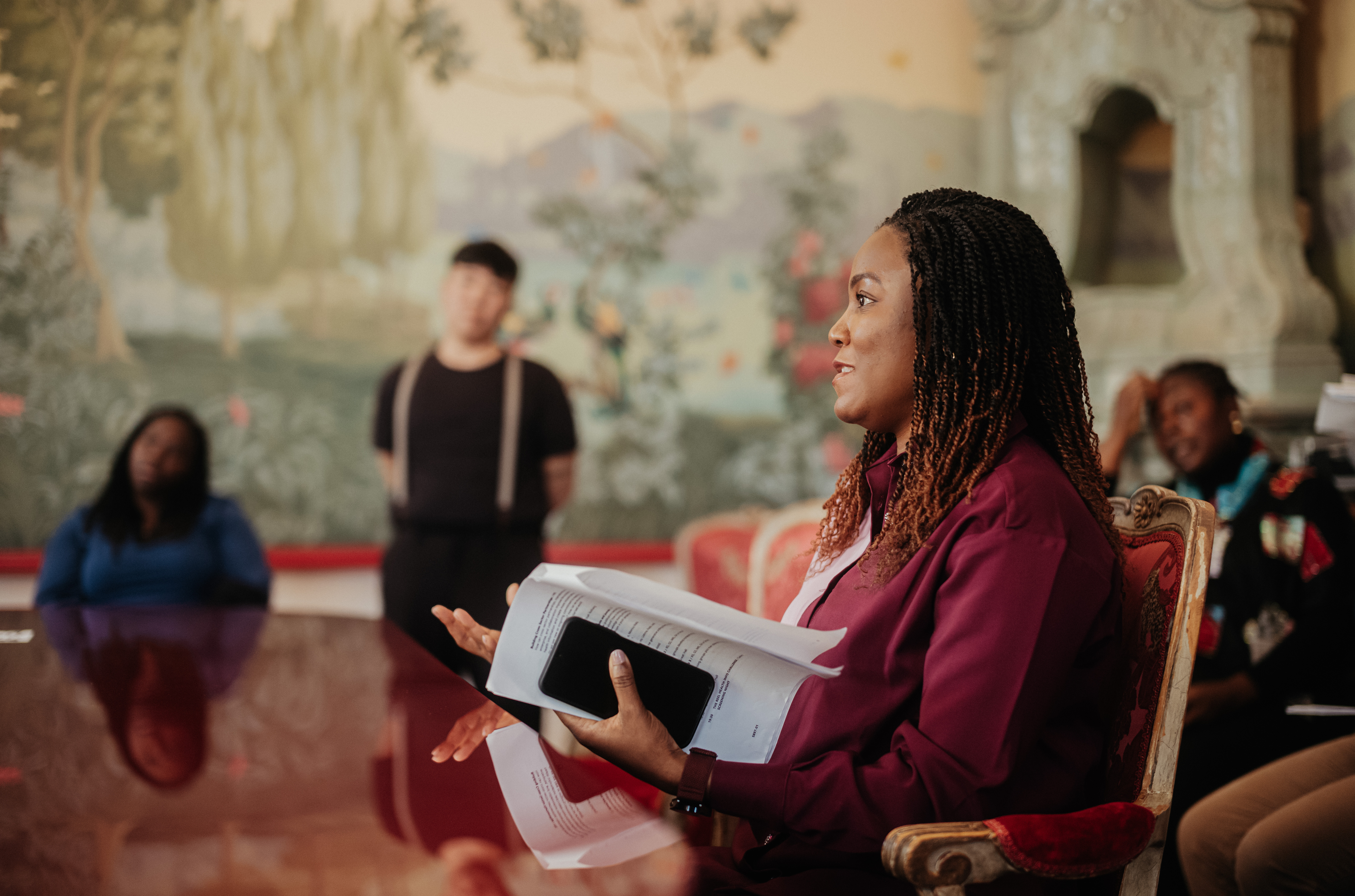 a woman sitting at a table and holding a notebook and looking into the distance off camera
