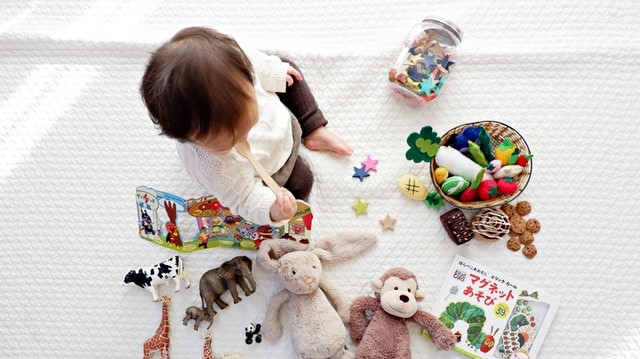 A toddler sits surrounded by books and toys