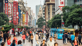 a busy street in shanghai with tall buildings and shop signs, filled with people walking.